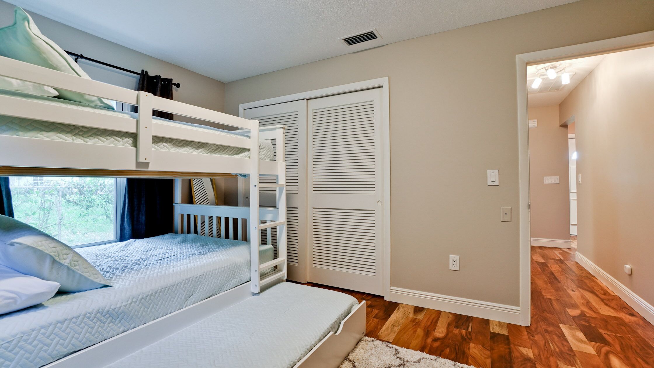 A bunk bed room with a window, a closet, and a hallway.