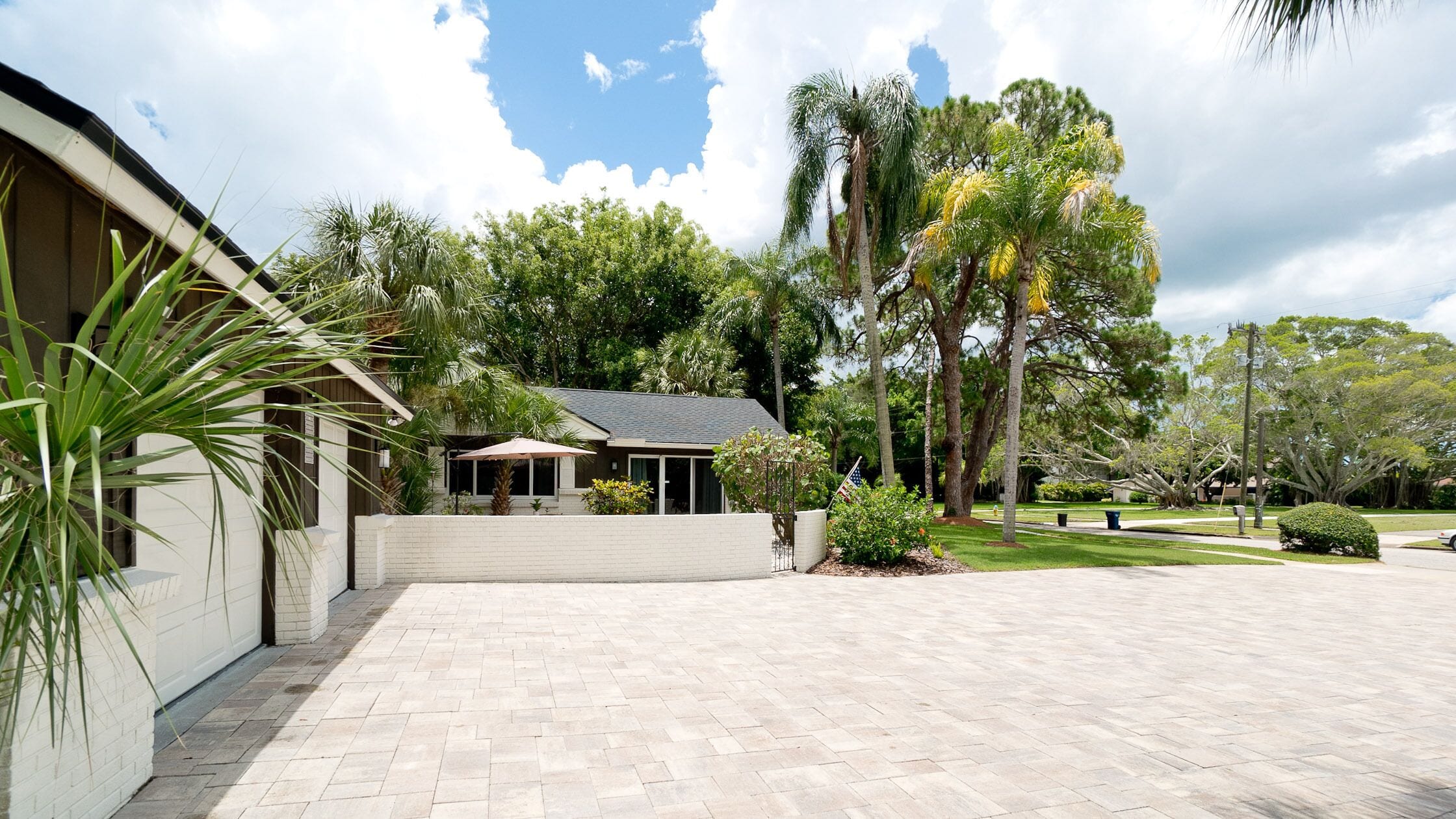A spacious courtyard with a paved walkway, surrounded by lush greenery and tall trees.