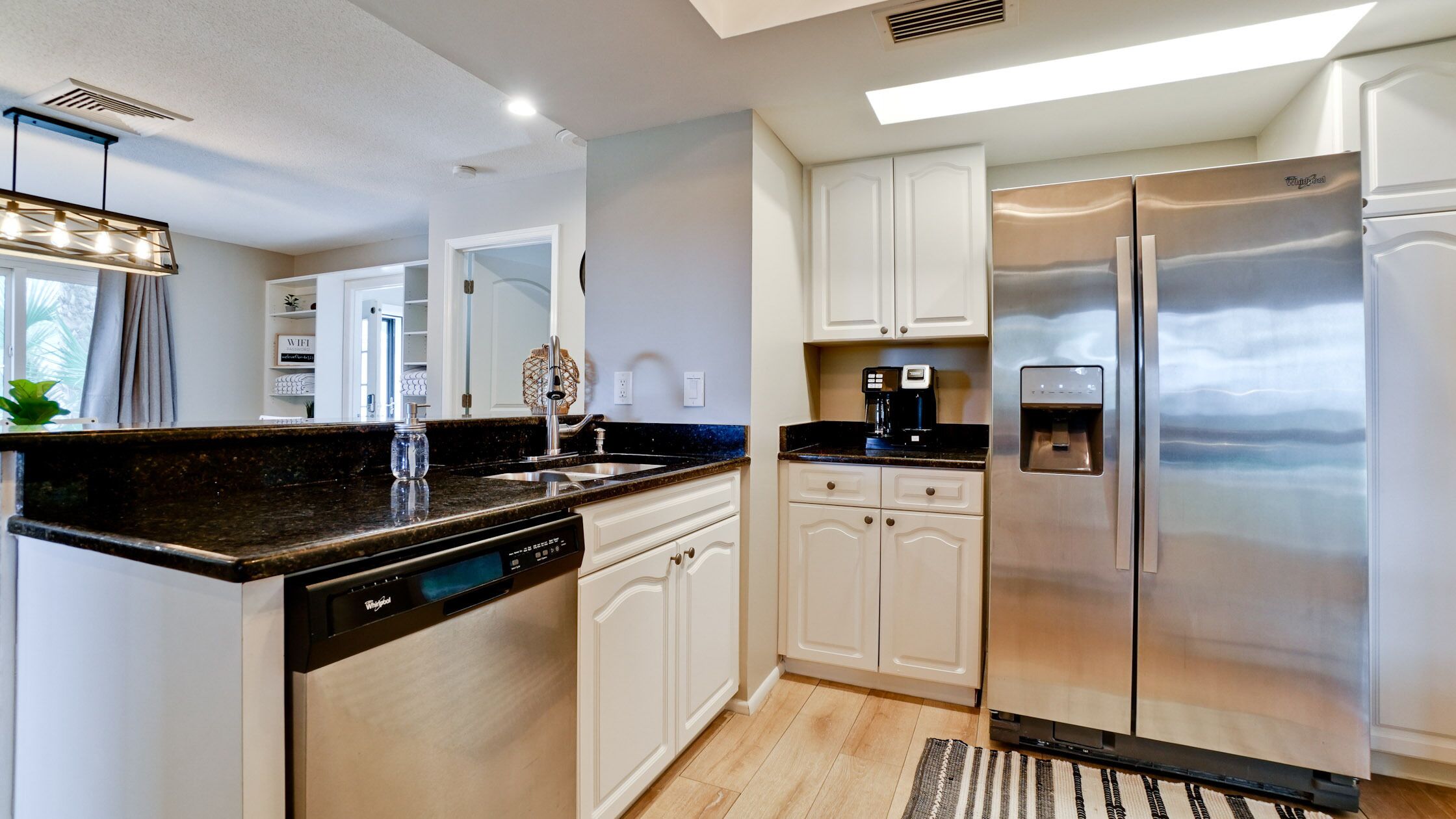 Una cocina moderna con gabinetes blancos, refrigerador de acero inoxidable, lavavajillas integrado y cafetera.