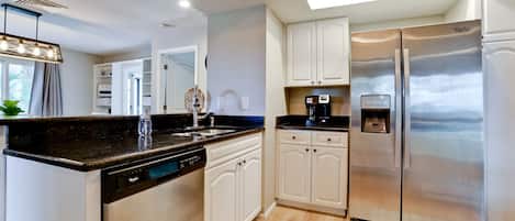 Una cocina moderna con gabinetes blancos, refrigerador de acero inoxidable, lavavajillas integrado y cafetera.