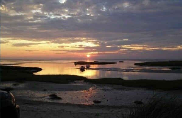 A sunset over a calm water body with boats and a distant shoreline.