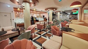 A modern interior with round tables and cushioned seating, a central counter with a display case, and a patterned floor. - Lazy Days Adults Only Duna Parque Resorts & Hotels (Odemira)