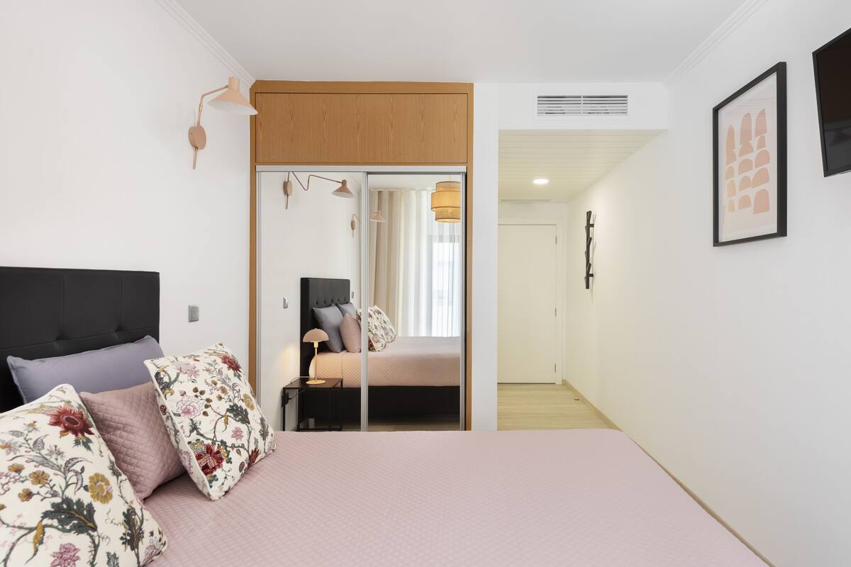 Een slaapkamer met een bed, een nachtkastje, een lamp en een deur naar een andere kamer.