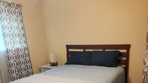 A bedroom with a bed, a nightstand, a lamp, and a patterned curtain. - Single Family Home 3 bedroom 2 bath (San Angelo)