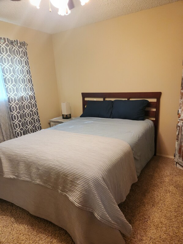 Un dormitorio con cama, mesita de noche, lámpara y cortina estampada.