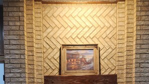 A fireplace with a herringbone brick pattern, a framed painting above it, and a basket to the right. - Single Family Home 3 bedroom 2 bath (San Angelo)