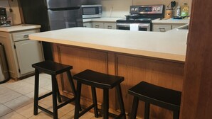 A kitchen with a large island, three stools, a refrigerator, a microwave, and a stove. - Single Family Home 3 bedroom 2 bath (San Angelo)