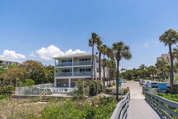 Um hotel com vários andares, varandas, piscina e calçadão que leva à praia.