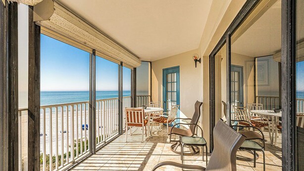 A balcony with a view of the beach, outdoor furniture, and a door with a blue frame.