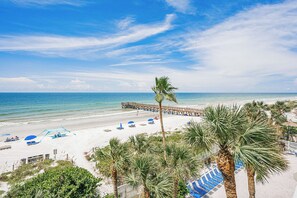 A beach with a wooden pier extending into the ocean, palm trees, and beach umbrellas.