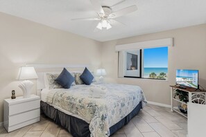 Une chambre à coucher comprenant un lit, des tables de chevet, un ventilateur de plafond, une fenêtre avec vue et un téléviseur.