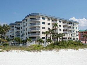 A multi-story hotel with balconies, located near a sandy beach with palm trees. - Beach Palms 310 - GULF VIEW Condo! (Indian Shores)