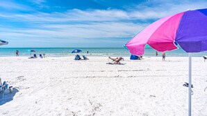 Een strand met wit zand, een helderblauwe lucht en enkele parasols.