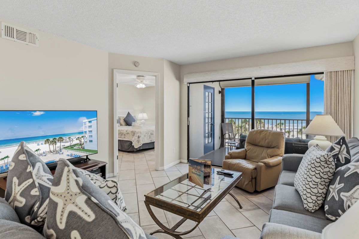 A living room with a television, a sofa, a coffee table, and a view of the beach.
