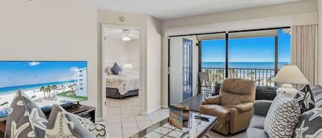 A living room with a television, a sofa, a coffee table, and a view of the beach.