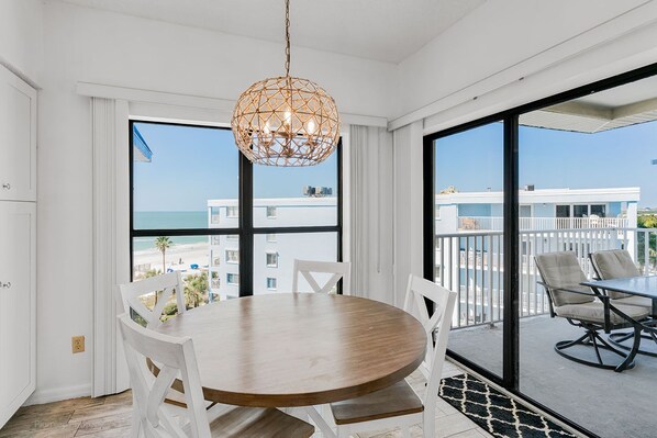 Enjoy a meal at the round dining table surrounded by comfortable chairs, with a view of the beach and a nearby building.