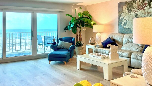 Ein großzügiger Wohnraum mit Meerblick, ein blauer Sessel, ein weißer Couchtisch und ein beiges Sofa.