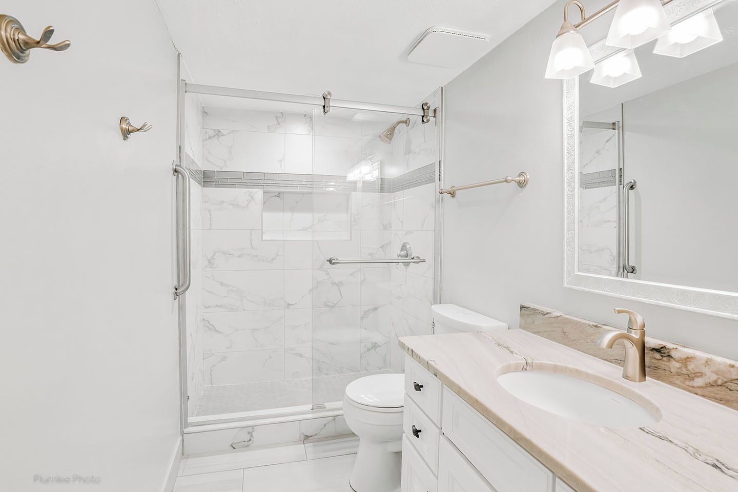 Et moderne badeværelse med glasvæg omkring brusebad, et hvidt toilet, en marmorvaskebord med håndvask og et stort spejl.