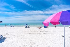 A beach with white sand, clear blue sky, and a few umbrellas.