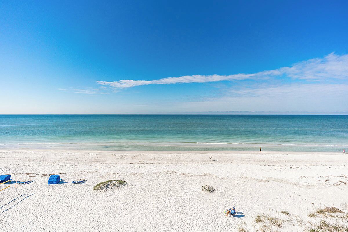 A beach with white sand, clear blue water, and a few people in the distance.