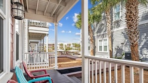 A covered porch with colorful Adirondack chairs, a wooden deck, and a view of a residential area with palm trees and a building with a white facade. - Fall Rates! | Pool | Foosball | Dog Friendly (Mexico Beach)