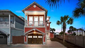 A two-story house with a red exterior, a balcony on the upper floor, and a garage with a wooden door. - Fall Rates! | Pool | Foosball | Dog Friendly (Mexico Beach)