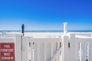 A beach view with a white fence and a sign that reads "POOL FURNITURE MUST REMAIN IN RECREATION AREA."