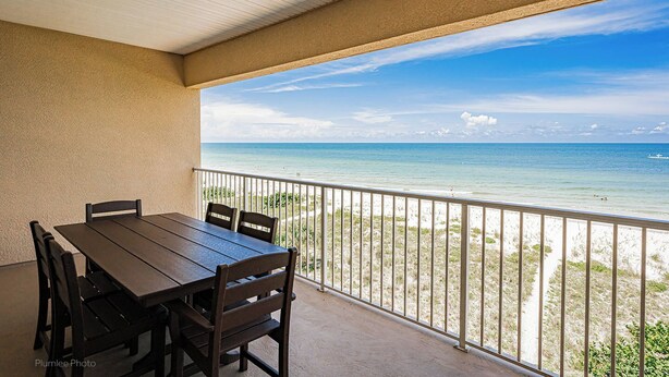 A covered outdoor area with a table and chairs, overlooking a beach with clear blue water and a sandy shore. - Direct GULF front Condo - Oceanway 403 (Indian Rocks Beach)