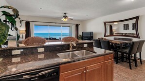 A modern kitchen with granite countertops, a built-in dishwasher, and a dining area with a view of the ocean. - Direct GULF front Condo - Oceanway 403 (Indian Rocks Beach)