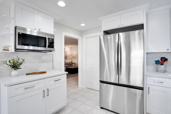 A modern kitchen with white cabinetry, stainless steel appliances, and a marble countertop.