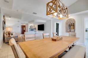 A spacious dining area with a wooden table and chairs, a chandelier, and a view of the kitchen in the background. - Ohana House 333 - Intercoastal Views with a Pool (Indian Rocks Beach)