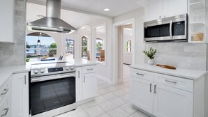 A modern kitchen with white cabinetry, stainless steel appliances, and a view to the outside. - Ohana House 333 - Intercoastal Views with a Pool (Indian Rocks Beach)