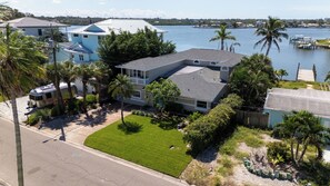 A residential area with a house featuring a large lawn, a dock, and a view of a body of water. - Ohana House 333 - Intercoastal Views with a Pool (Indian Rocks Beach)