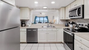 A modern kitchen with white cabinets, stainless steel appliances, and a view to the outside. - Gulf-Front 3BR | Pool & Sunsets | Reef Club 310 (Indian Rocks Beach)