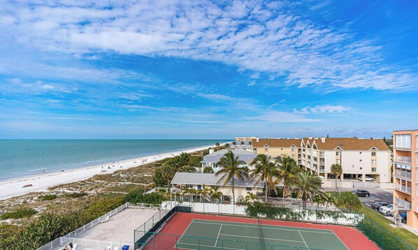 A beachfront property with a tennis court, beach access, and multiple-story buildings.