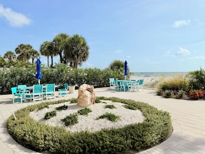 A circular seating area with a central rock feature, surrounded by a hedge, and overlooking a beach.