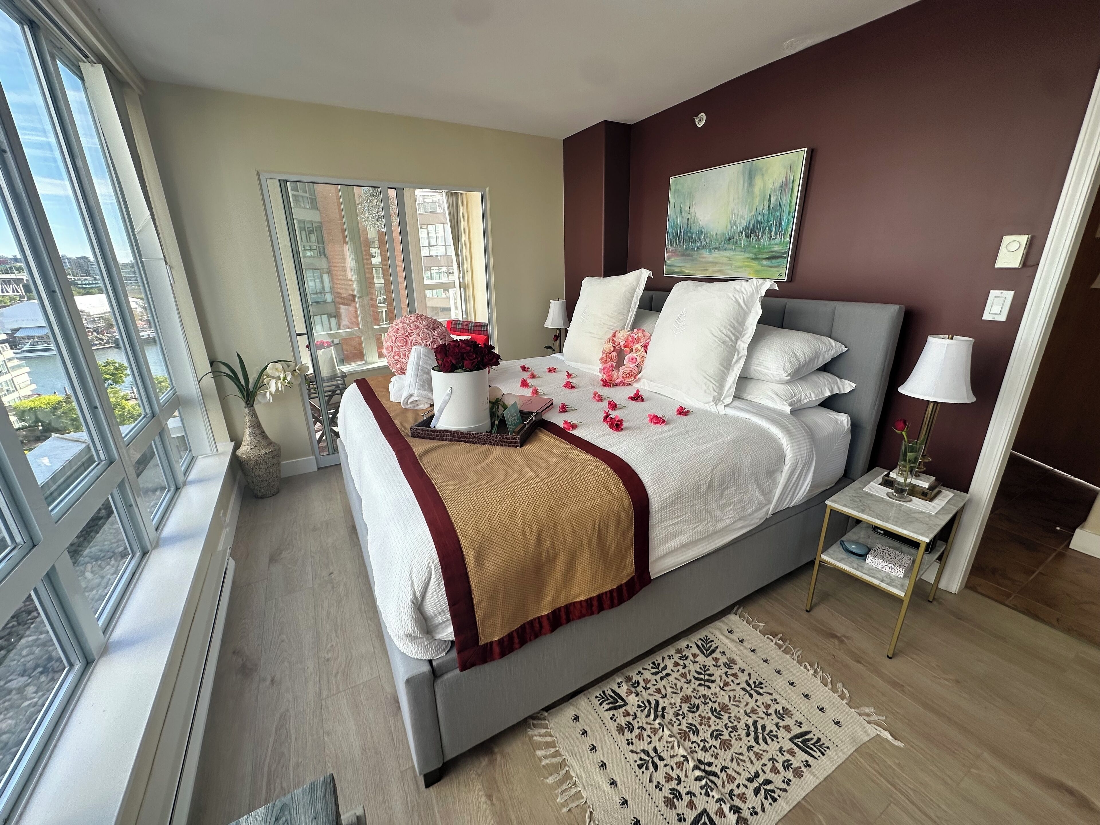A modern bedroom with a large bed, a bedside table, a nightstand, a window, and a view of the city.