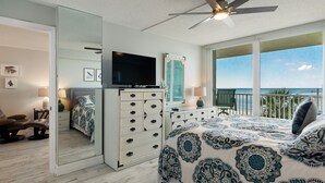 Une chambre dotée d’un grand lit, d’une télévision, d’une commode et d’un balcon offrant une vue sur l’océan.