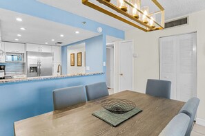 Une cuisine moderne dotée d’appareils électroménagers en acier inoxydable, d’un mur d’accent bleu et d’un coin repas avec une table en bois et des chaises bleues.