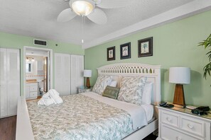 Une chambre à coucher comprenant un lit, des tables de chevet, un ventilateur de plafond et une armoire.