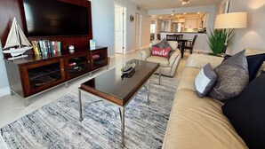 Ein Wohnzimmer mit Flachbildfernseher, Couchtisch, Sofa und Essbereich im Hintergrund.