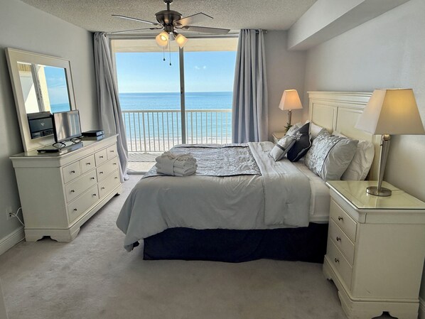 Une chambre à coucher avec un lit, des tables de chevet, une commode, un ventilateur de plafond et une vue sur la mer.