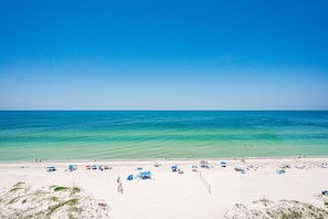 Ein Strand mit klarem türkisblauem Wasser, weißem Sand und mehreren Sonnenschirmen und Liegestühlen.
