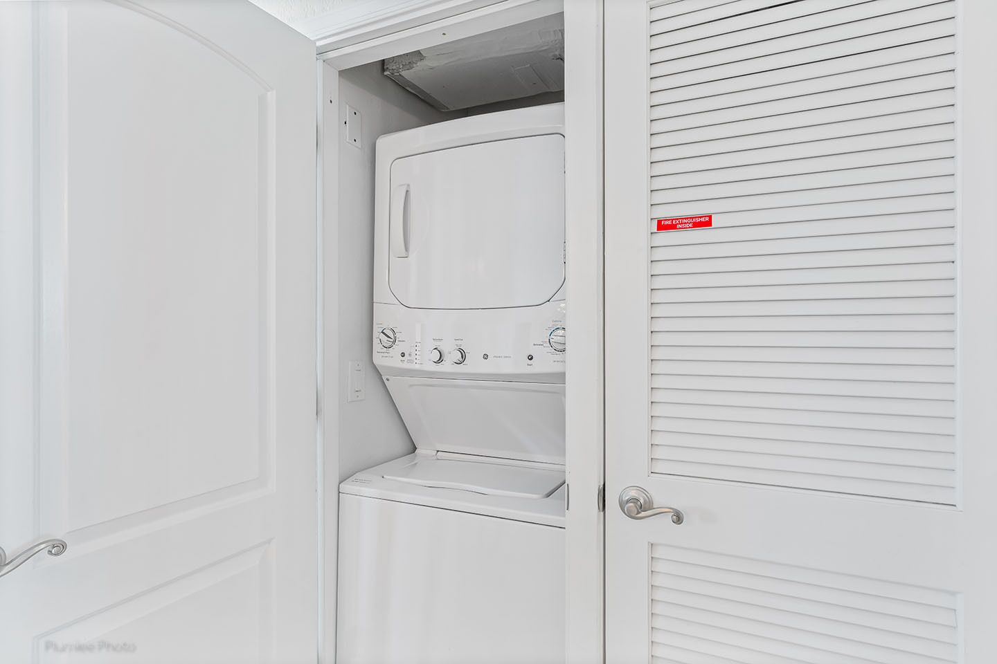 A laundry room with a white washing machine and dryer, a fire extinguisher sign, and a door with a handle.