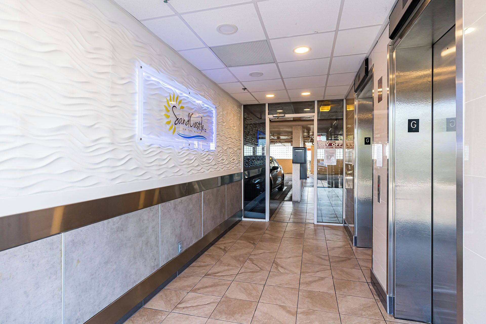 A hotel corridor with a reception area, a car parked outside, and an elevator.