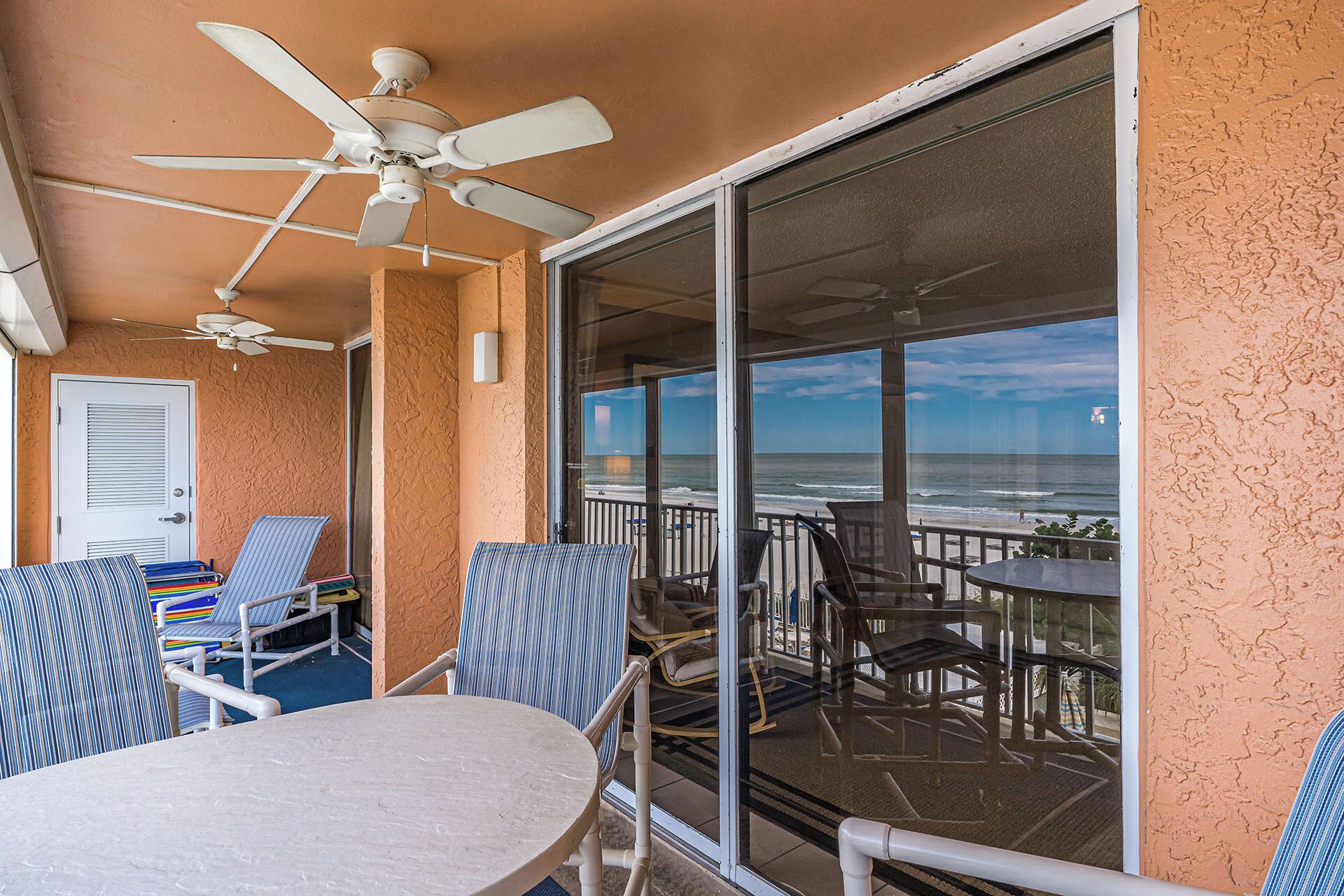 Un balcon avec une table et des chaises, un ventilateur de plafond et une vue sur la plage.