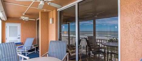 A balcony with a table and chairs, a ceiling fan, and a view of the beach.