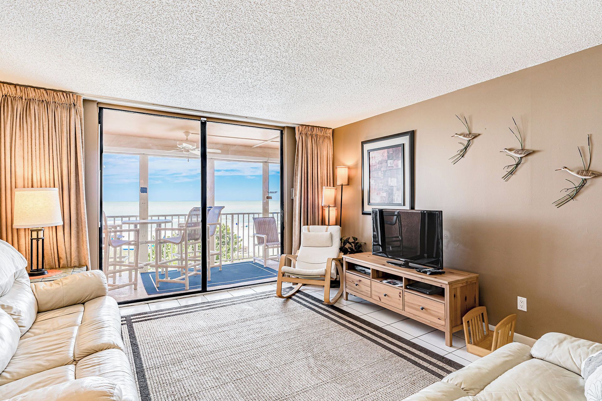 Een hotelkamer met balkon, televisie, bank en houten kast.