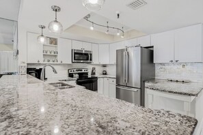 A modern kitchen with white cabinetry, granite countertops, stainless steel appliances, pendant lighting, and a backsplash with glass tiles.