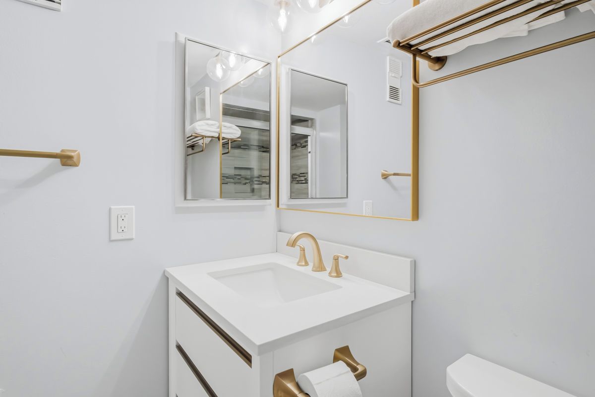 Ein Badezimmer mit einem weißen Waschbecken, goldenen Armaturen, einem Spiegel und einem Handtuchhalter.